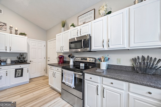 kitchen featuring light wood-type flooring, vaulted ceiling, white cabinets, and appliances with stainless steel finishes