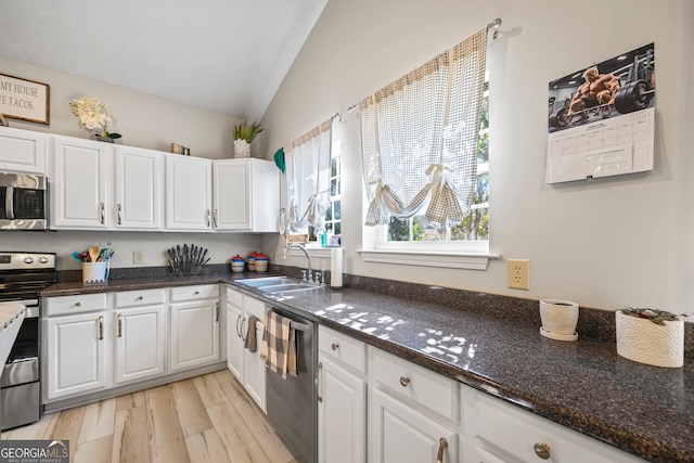 kitchen featuring lofted ceiling, sink, appliances with stainless steel finishes, white cabinetry, and dark stone counters