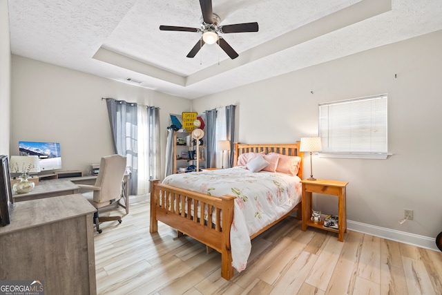 bedroom featuring ceiling fan, a raised ceiling, a textured ceiling, and light wood-type flooring