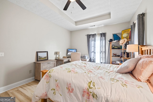 bedroom with ceiling fan, light hardwood / wood-style flooring, a raised ceiling, and a textured ceiling