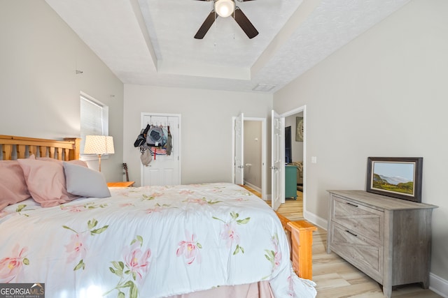 bedroom with a raised ceiling, ceiling fan, and light hardwood / wood-style flooring