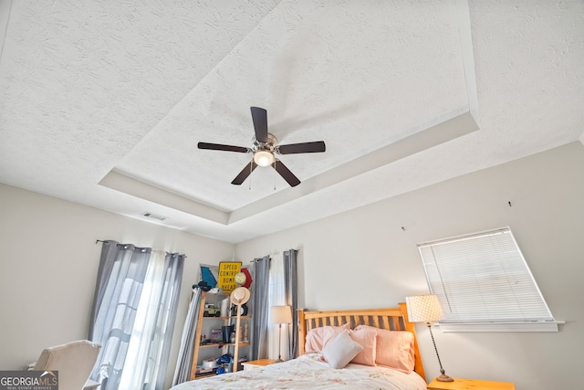 bedroom with ceiling fan, a raised ceiling, and a textured ceiling