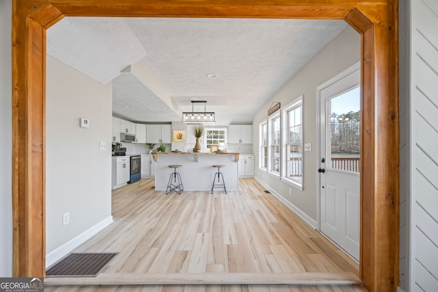 kitchen featuring pendant lighting, light hardwood / wood-style flooring, a breakfast bar, white cabinetry, and range with electric stovetop