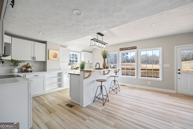 kitchen with decorative backsplash, white cabinets, a kitchen island, decorative light fixtures, and light wood-type flooring