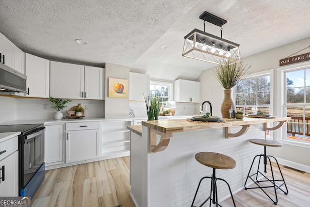 kitchen featuring decorative light fixtures, butcher block counters, white cabinets, a kitchen breakfast bar, and black / electric stove