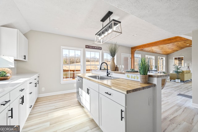 kitchen with sink, white cabinetry, vaulted ceiling, hanging light fixtures, and an island with sink