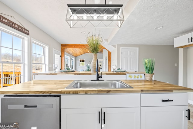 kitchen with wood counters, sink, white cabinets, stainless steel dishwasher, and a textured ceiling