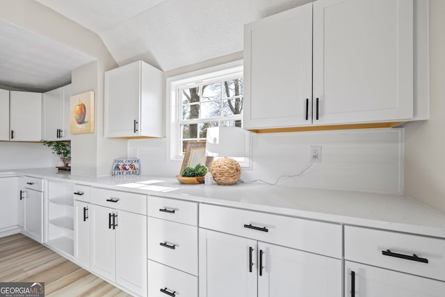 kitchen featuring light stone counters, a textured ceiling, white cabinets, and light wood-type flooring