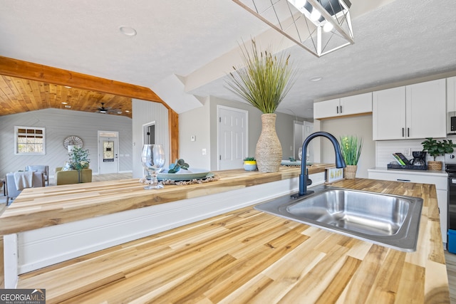 kitchen featuring white cabinetry, sink, vaulted ceiling with beams, and butcher block counters