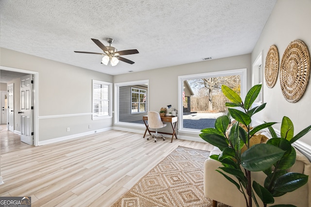 living area with ceiling fan, light hardwood / wood-style floors, and a textured ceiling