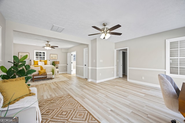 living room with ceiling fan, a textured ceiling, and light hardwood / wood-style floors