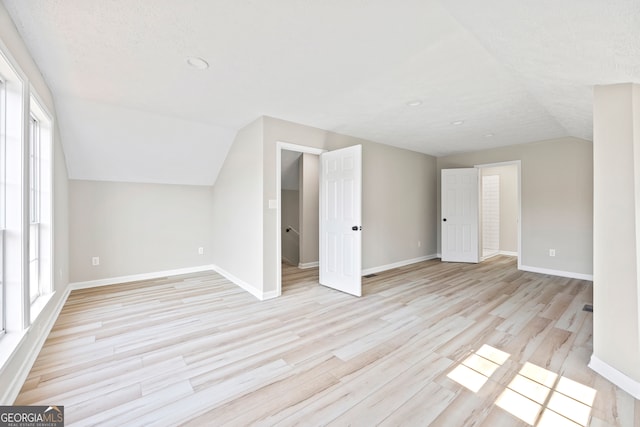 bonus room with plenty of natural light, vaulted ceiling, a textured ceiling, and light wood-type flooring