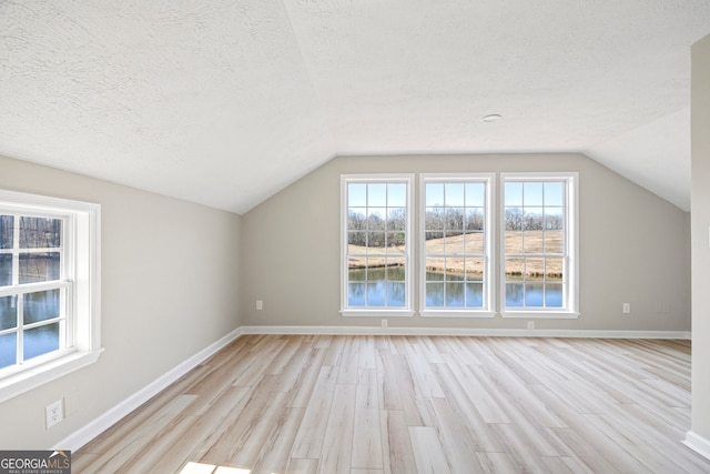 additional living space with vaulted ceiling, light hardwood / wood-style floors, a textured ceiling, and a water view