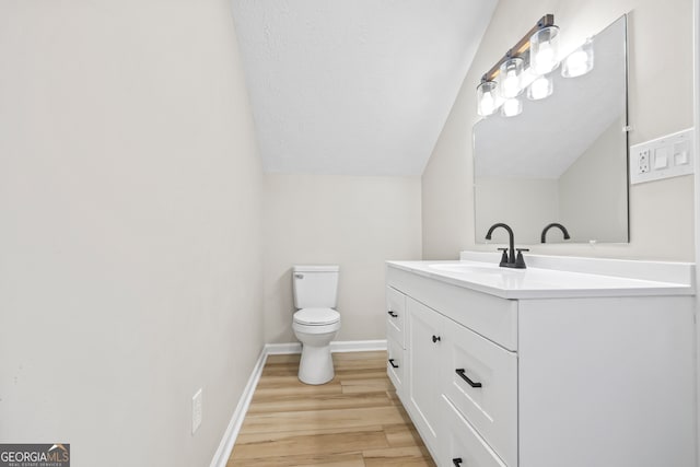 bathroom with vaulted ceiling, wood-type flooring, vanity, toilet, and a textured ceiling