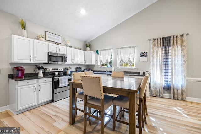 kitchen featuring lofted ceiling, light hardwood / wood-style floors, white cabinets, and appliances with stainless steel finishes