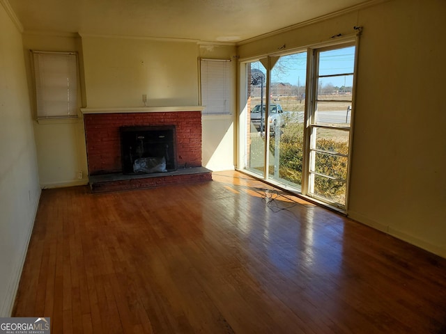 unfurnished living room with wood-type flooring, a brick fireplace, and crown molding