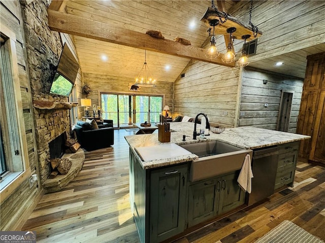 kitchen with light stone counters, sink, decorative light fixtures, and a center island with sink