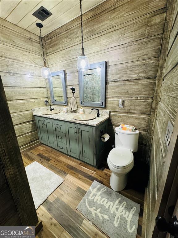 bathroom featuring wood-type flooring, toilet, vanity, and wood walls