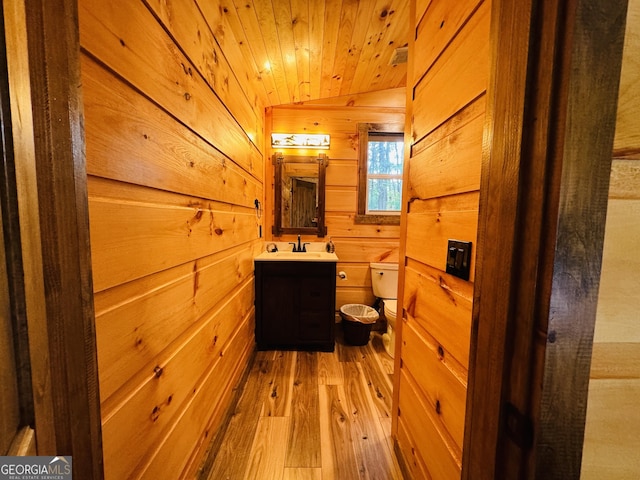 bathroom with hardwood / wood-style floors, wooden walls, vanity, wooden ceiling, and toilet