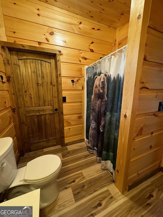 bathroom featuring wood-type flooring, wooden walls, and toilet