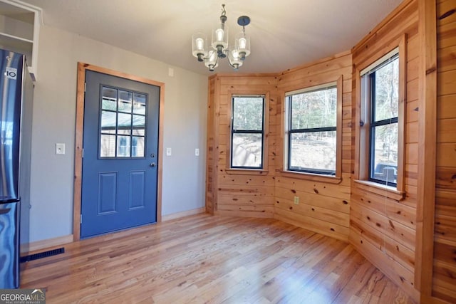 interior space with an inviting chandelier, light hardwood / wood-style flooring, and wood walls