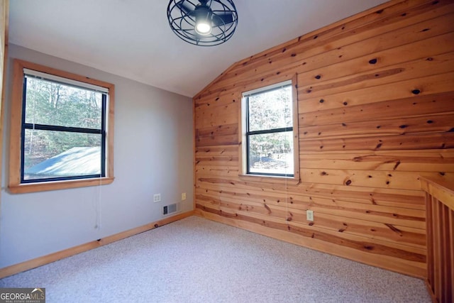 carpeted spare room featuring lofted ceiling and wooden walls