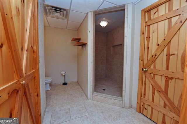 bathroom with a paneled ceiling, a tile shower, tile patterned floors, and toilet