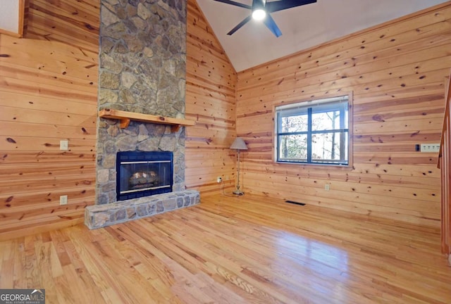 unfurnished living room with a stone fireplace, wood walls, high vaulted ceiling, ceiling fan, and hardwood / wood-style floors