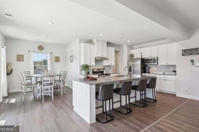 kitchen with stainless steel appliances, a breakfast bar, a kitchen island with sink, and white cabinets