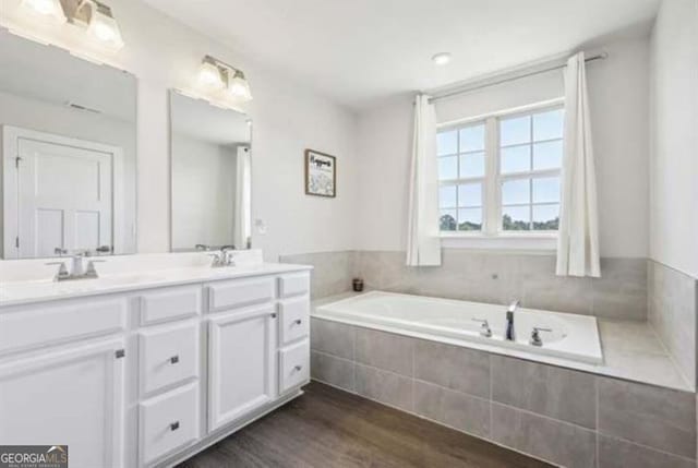 bathroom with a relaxing tiled tub, vanity, and wood-type flooring