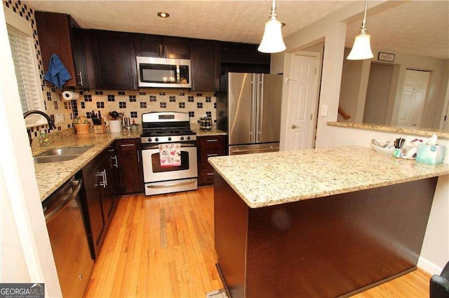 kitchen featuring sink, appliances with stainless steel finishes, hanging light fixtures, light hardwood / wood-style floors, and kitchen peninsula