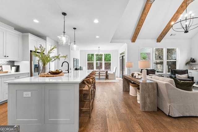 kitchen with decorative light fixtures, beamed ceiling, white cabinetry, hardwood / wood-style flooring, and a spacious island