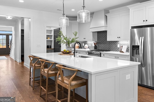 kitchen featuring premium range hood, a kitchen island with sink, white cabinetry, stainless steel appliances, and a kitchen breakfast bar