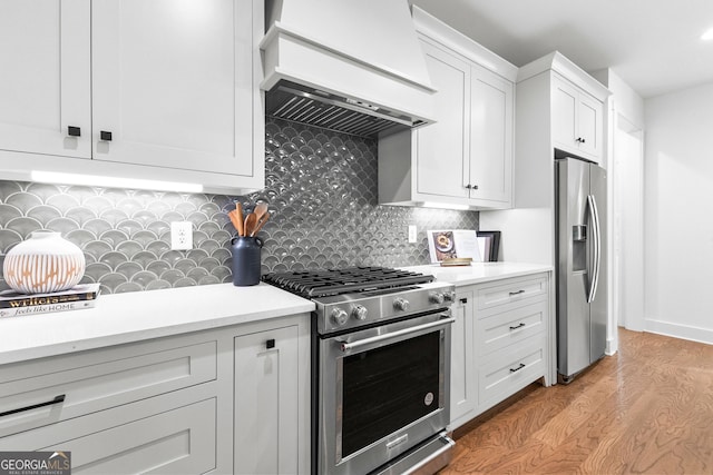 kitchen with tasteful backsplash, white cabinets, light hardwood / wood-style floors, stainless steel appliances, and custom range hood