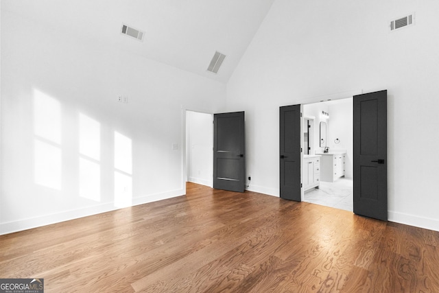 unfurnished bedroom with light hardwood / wood-style flooring, high vaulted ceiling, and ensuite bathroom