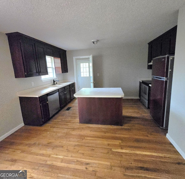 kitchen featuring sink, a center island, dark brown cabinetry, stainless steel appliances, and light wood-type flooring