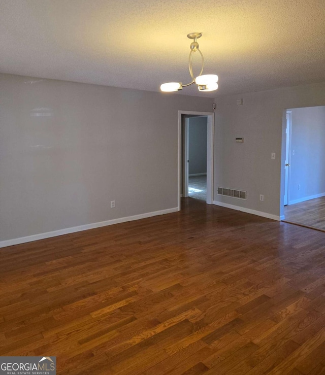 empty room featuring a chandelier, a textured ceiling, and dark hardwood / wood-style flooring