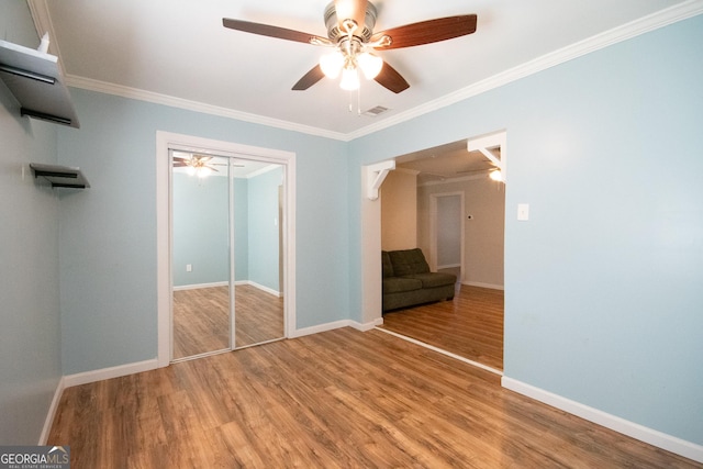 unfurnished bedroom featuring wood-type flooring, ceiling fan, crown molding, and a closet