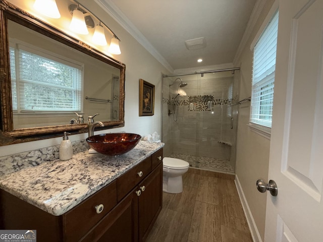 bathroom with a wealth of natural light, a shower with shower door, ornamental molding, vanity, and toilet