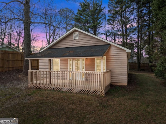 rear view of property featuring a yard, roof with shingles, and fence