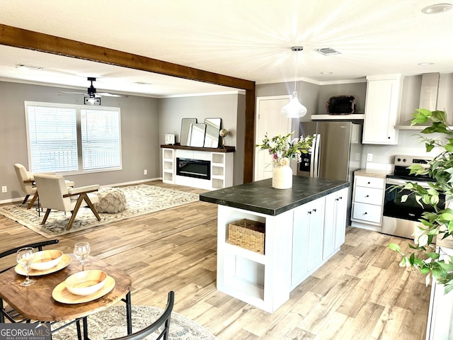 kitchen featuring decorative light fixtures, a center island, appliances with stainless steel finishes, white cabinets, and wall chimney range hood