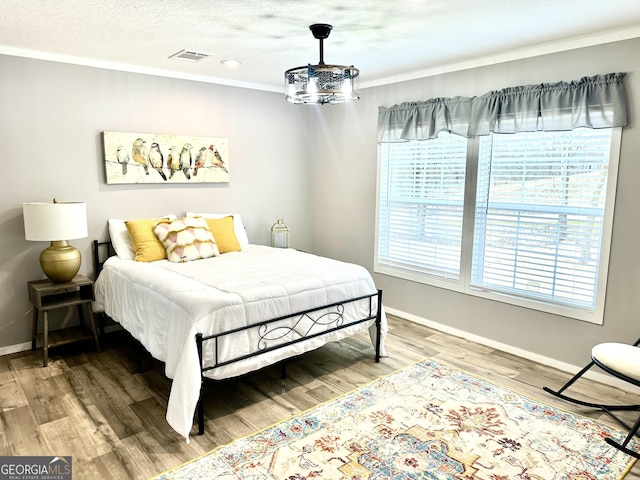 bedroom featuring crown molding, wood-type flooring, a chandelier, and a textured ceiling