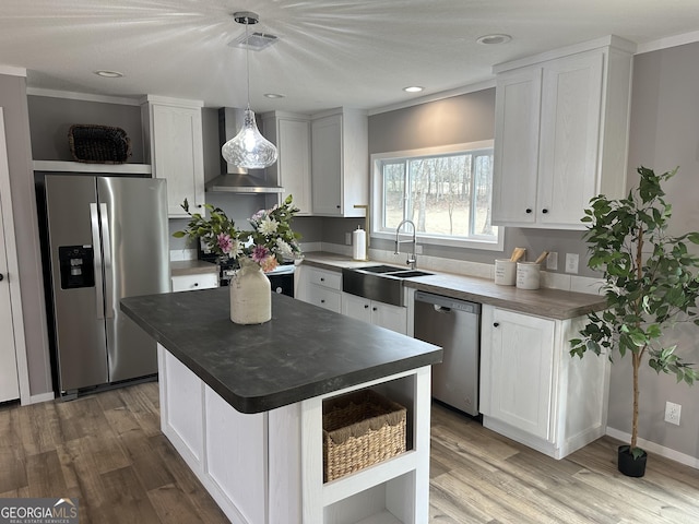 kitchen featuring wall chimney range hood, sink, appliances with stainless steel finishes, white cabinets, and decorative light fixtures