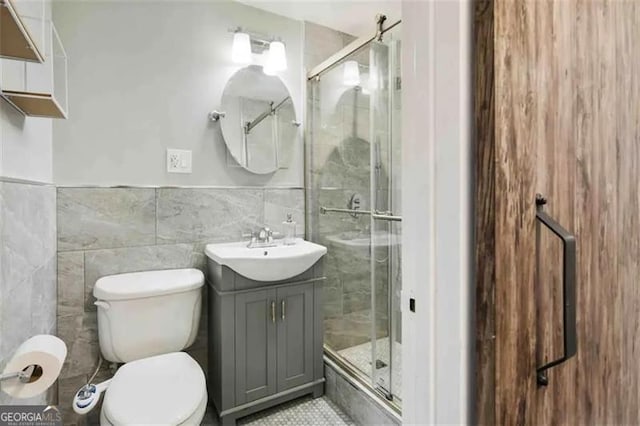 bathroom with vanity, a shower with shower door, tile walls, and toilet