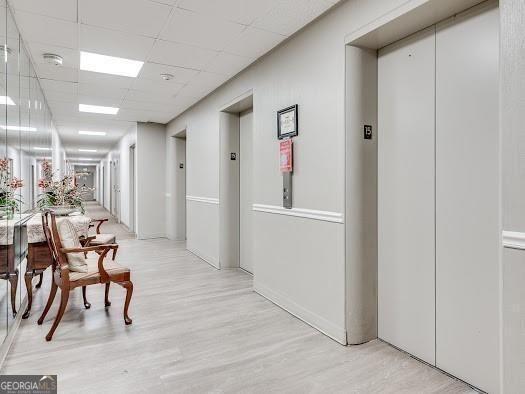 hall with a paneled ceiling, elevator, and light wood-type flooring