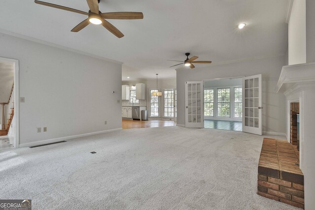 unfurnished living room with ornamental molding, carpet flooring, a fireplace, and french doors