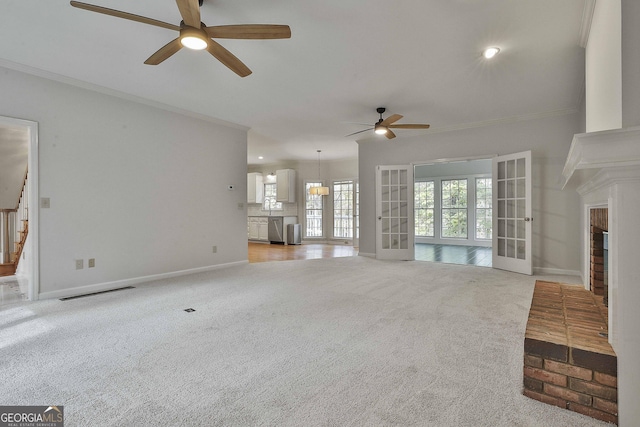 unfurnished living room featuring french doors, light colored carpet, ornamental molding, and a fireplace