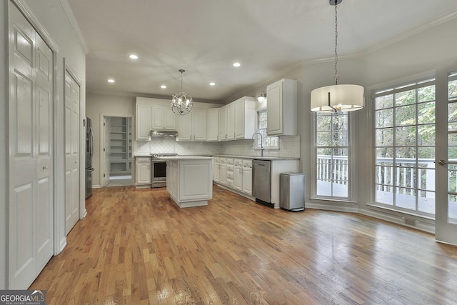 kitchen with appliances with stainless steel finishes, white cabinetry, a center island, ornamental molding, and decorative light fixtures