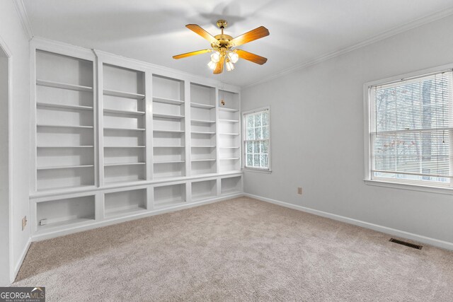 spare room with built in shelves, ceiling fan, ornamental molding, and carpet