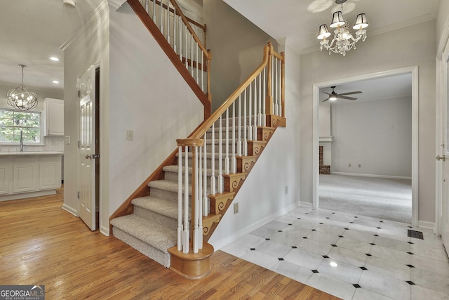 stairway featuring sink, ceiling fan with notable chandelier, ornamental molding, and hardwood / wood-style floors